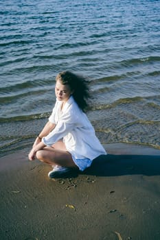 lovely young woman with curly hair, the romance of youth, a journey walk on a warm summer sunny day on a sandy beach with water
