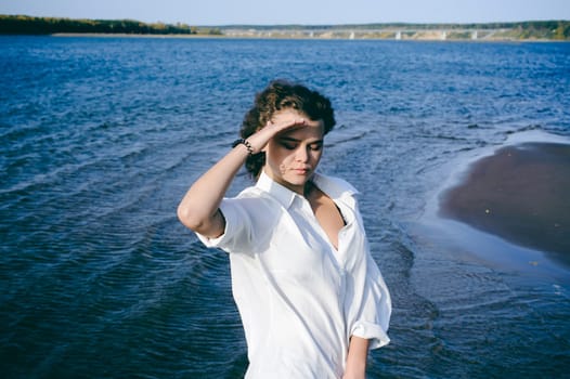 lovely young woman with curly hair, the romance of youth, a journey walk on a warm summer sunny day on a sandy beach with water
