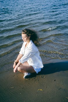 lovely young woman with curly hair, the romance of youth, a journey walk on a warm summer sunny day on a sandy beach with water