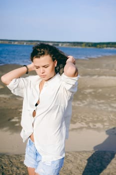 lovely young woman with curly hair, the romance of youth, a journey walk on a warm summer sunny day on a sandy beach with water