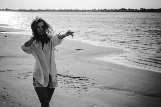 lovely young woman with curly hair, the romance of youth, a journey walk on a warm summer sunny day on a sandy beach with water