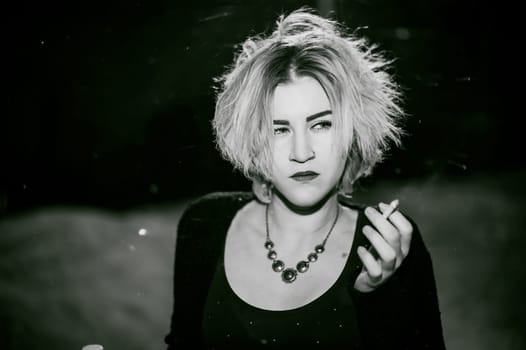 Black and white portrait of a girl with a cigarette. young beautiful woman with dyed hair smoking a cigarette in the street under the snow