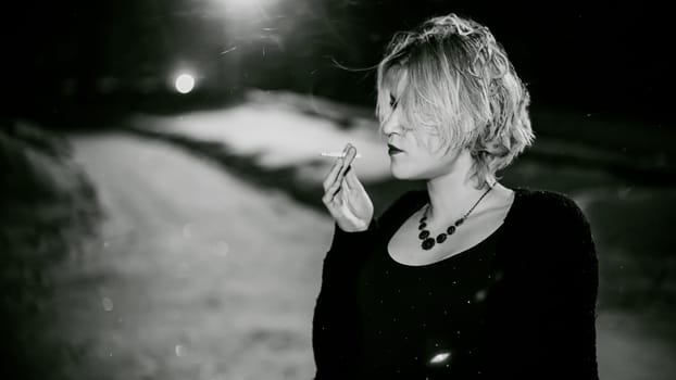 Black and white portrait of a girl with a cigarette. young beautiful woman with dyed hair smoking a cigarette in the street under the snow