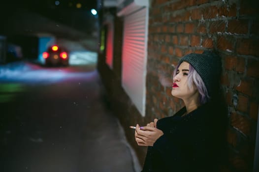 Portrait of a girl with a cigarette. young beautiful girl with dyed hair hipster hat. cigarette smoking on the street under the snow