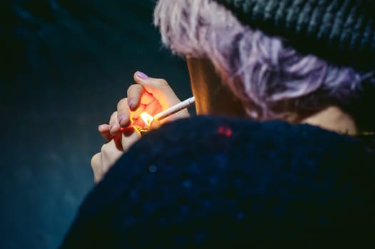 Portrait of a girl with a cigarette. young beautiful girl hipster with dyed hair smoking a cigarette in the street under the snow. her hands lights a lighter, lighting a cigarette tobacco