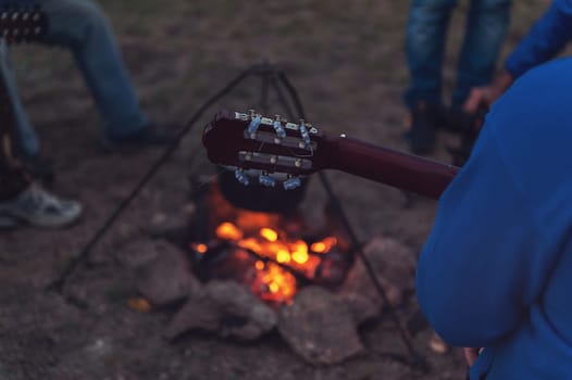 Closeup photo of the man playing o guitar near the campfire