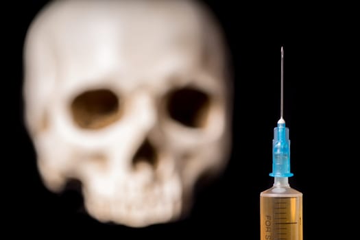 Syringe with brown liquid and blurry skull isolated on black background