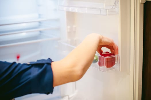 Housewives hand arranges purchased vegetables in the refrigerator