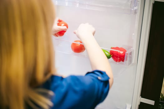 Housewives hand arranges purchased vegetables in the refrigerator
