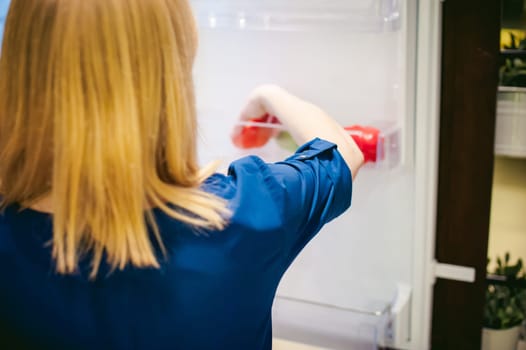 Housewives hand arranges purchased vegetables in the refrigerator