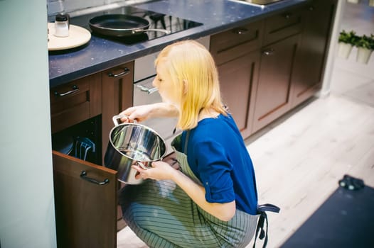 blonde woman with a pot in the kitchen. housewife in apron has been cooking in the kitchen, put pots and pans on the hob