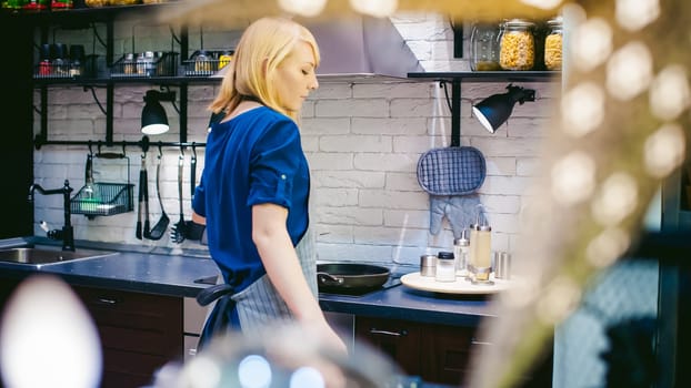 blonde woman with a pot in the kitchen. housewife in apron has been cooking in the kitchen, put pots and pans on the hob