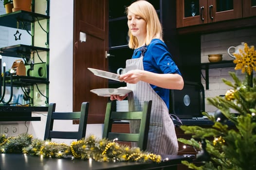 woman housewife setting the table. young blonde in a dress and apron, served in a dining table, puts the dishes, doing the work in the kitchen