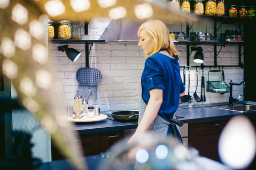 blonde woman with a pot in the kitchen. housewife in apron has been cooking in the kitchen, put pots and pans on the hob