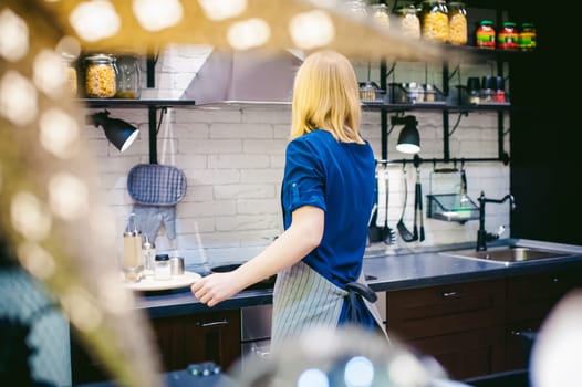blonde woman with a pot in the kitchen. housewife in apron has been cooking in the kitchen, put pots and pans on the hob