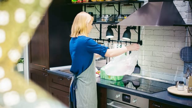 woman with shopping bags parses the kitchen. housewife in apron in the kitchen arranges bought food