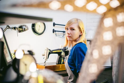 seamstress work on the sewing machine. young blonde woman working on a mechanical sewing machine at home sitting at your desk, be prepared to sew
