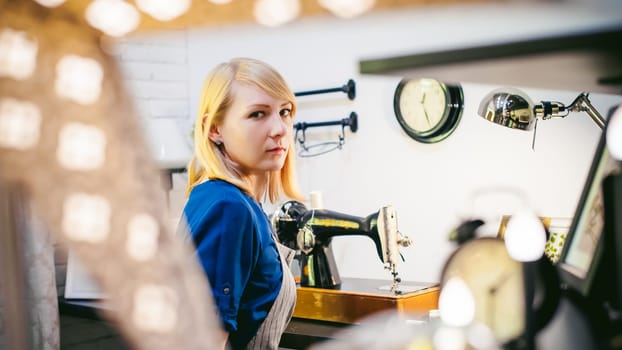 seamstress work on the sewing machine. young blonde woman working on a mechanical sewing machine at home sitting at your desk, be prepared to sew