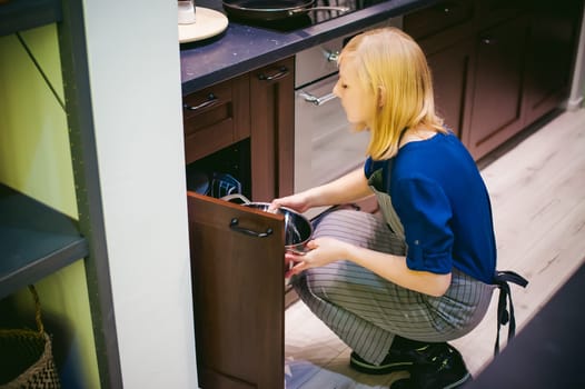 blonde woman with a pot in the kitchen. housewife in apron has been cooking in the kitchen, put pots and pans on the hob
