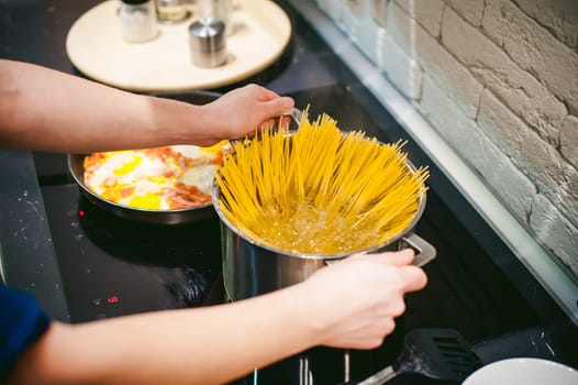 woman housewife preparing pasta in the kitchen. woman's hand dipped spaghetti in boiling water for cooking