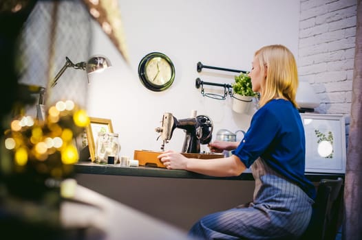 seamstress work on the sewing machine. young blonde woman working on a mechanical sewing machine at home sitting at your desk, be prepared to sew