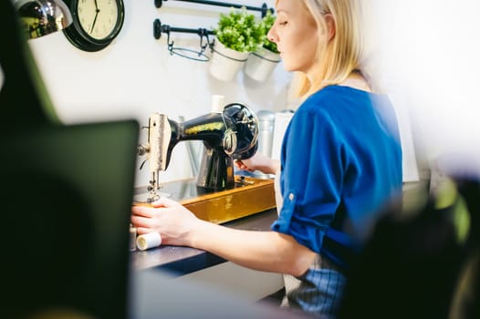 seamstress work on the sewing machine. young blonde woman working on a mechanical sewing machine at home sitting at your desk, be prepared to sew