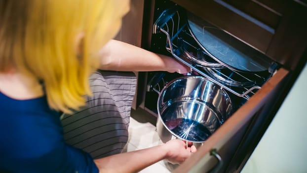 blonde woman with a pot in the kitchen. housewife in apron has been cooking in the kitchen, put pots and pans on the hob