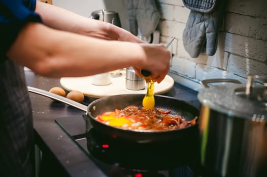 woman housewife prepares fried eggs with ham and vegetables in his kitchen. egg breaks, adding to the pan