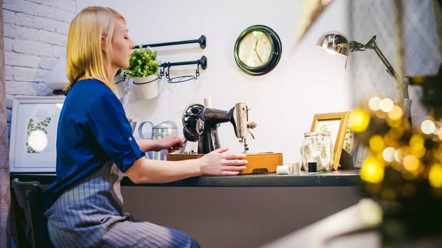 seamstress work on the sewing machine. young blonde woman working on a mechanical sewing machine at home sitting at your desk, be prepared to sew