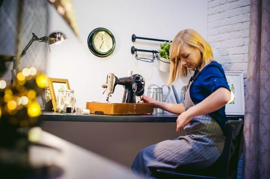 seamstress work on the sewing machine. young blonde woman working on a mechanical sewing machine at home sitting at your desk, be prepared to sew