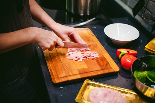 woman housewife prepares fried eggs with ham and vegetables in his kitchen. ham slices on the board and add to the pan