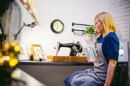 seamstress work on the sewing machine. young blonde woman working on a mechanical sewing machine at home sitting at your desk, be prepared to sew