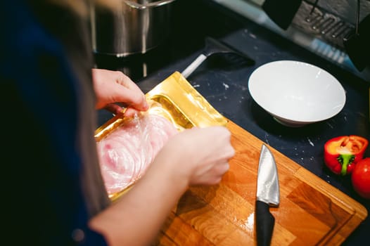 woman housewife prepares fried eggs with ham and vegetables in his kitchen. ham slices on the board and add to the pan