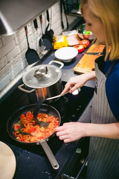 woman housewife prepares fried eggs with ham and vegetables in his kitchen. stir peppers and tomatoes in a pan