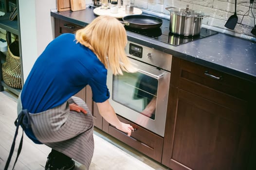 woman housewife in the kitchen. Girl is engaged in an apron kitchen chores, opened the shelf under the oven