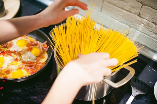 woman housewife preparing pasta in the kitchen. woman's hand dipped spaghetti in boiling water for cooking