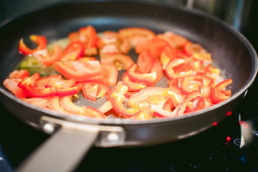 woman housewife prepares fried eggs with ham and vegetables in his kitchen. cut peppers and tomatoes, and puts them in a frying pan