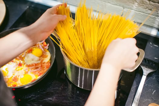 woman housewife preparing pasta in the kitchen. woman's hand dipped spaghetti in boiling water for cooking