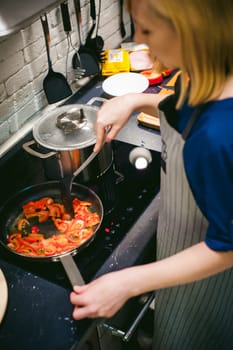 woman housewife prepares fried eggs with ham and vegetables in his kitchen. stir peppers and tomatoes in a pan