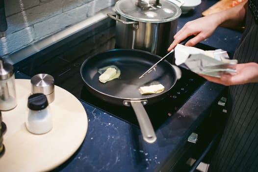 woman housewife prepares fried eggs with ham and vegetables in his kitchen. spreads the butter in the pan