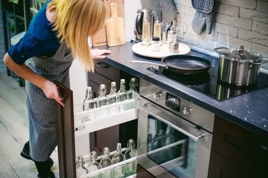 woman housewife in the kitchen. woman in an apron opened the shelf with empty bottles