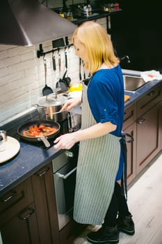 woman housewife prepares fried eggs with ham and vegetables in his kitchen. stir peppers and tomatoes in a pan