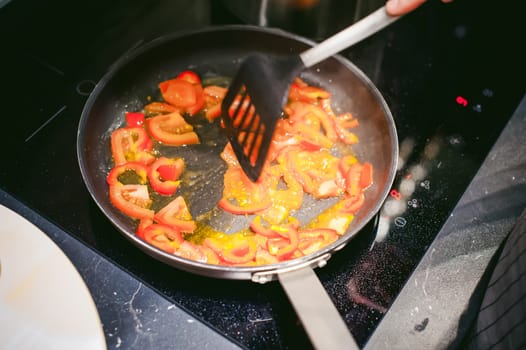 woman housewife prepares fried eggs with ham and vegetables in his kitchen. stir peppers and tomatoes in a pan