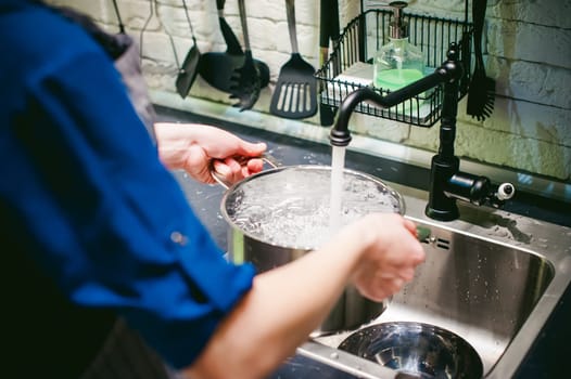 woman housewife in the kitchen. girl collects water from the tap in the pan