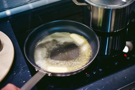 woman housewife prepares fried eggs with ham and vegetables in his kitchen. spreads the butter in the pan