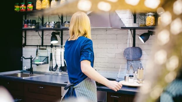 blonde woman with a pot in the kitchen. housewife in apron has been cooking in the kitchen, put pots and pans on the hob