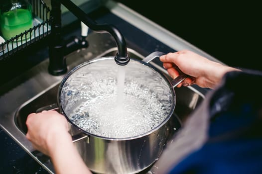 woman housewife in the kitchen. girl collects water from the tap in the pan