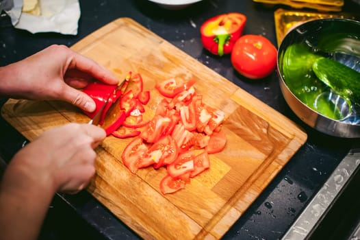 woman housewife prepares fried eggs with ham and vegetables in his kitchen. cut peppers and tomatoes, and puts them in a frying pan