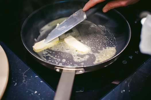 woman housewife prepares fried eggs with ham and vegetables in his kitchen. spreads the butter in the pan