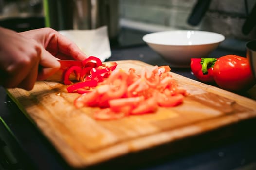 woman housewife prepares fried eggs with ham and vegetables in his kitchen. cut peppers and tomatoes, and puts them in a frying pan